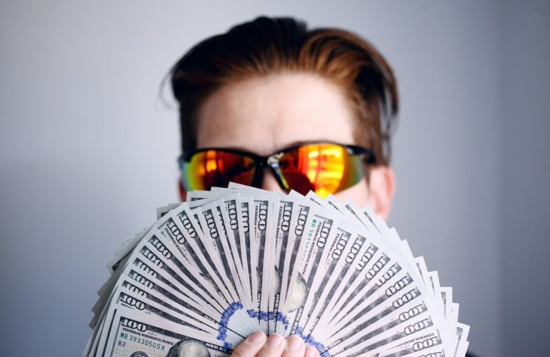 A man partially covering his face with cash.